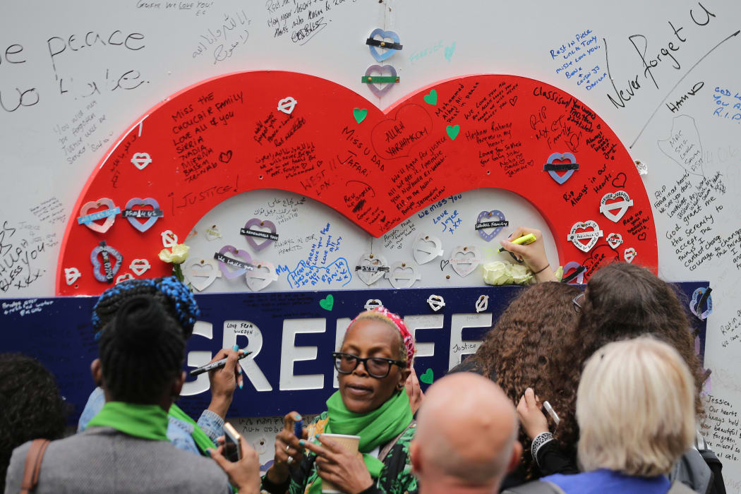 People write messages on a memorial wall near Grenfell Tower on the anniversary of the Grenfell fire in West London.