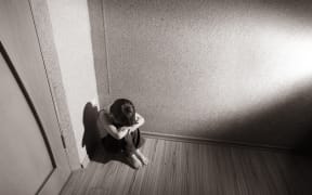 A young boy sits in the corner with his head in his hands (file photo)