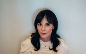 Author Emily Perkins sitting wearing a cream coloured blouse and black skirt.