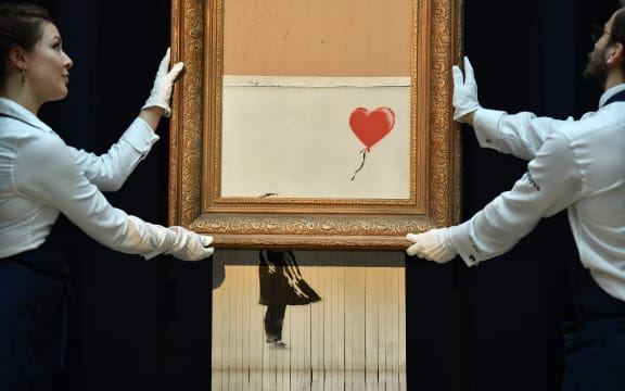 Sotheby's employees pose with the newly completed work by artist Banksy entitled "Love is in the Bin", a work that was created when the painting "Girl with Balloon" was passed through a shredder in a surprise intervention by the artist, at Sotheby's auction house in London.