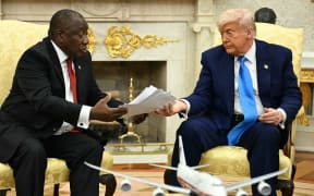 US President Donald Trump hands papers to South African President Cyril Ramaphosa during a meeting in the Oval Office of the White House in Washington, DC, on May 21, 2025. South African President Cyril Ramaphosa meets Donald Trump on Wednesday amid tensions over Washington's resettlement of white Afrikaners that the US president claims are the victims of "genocide."