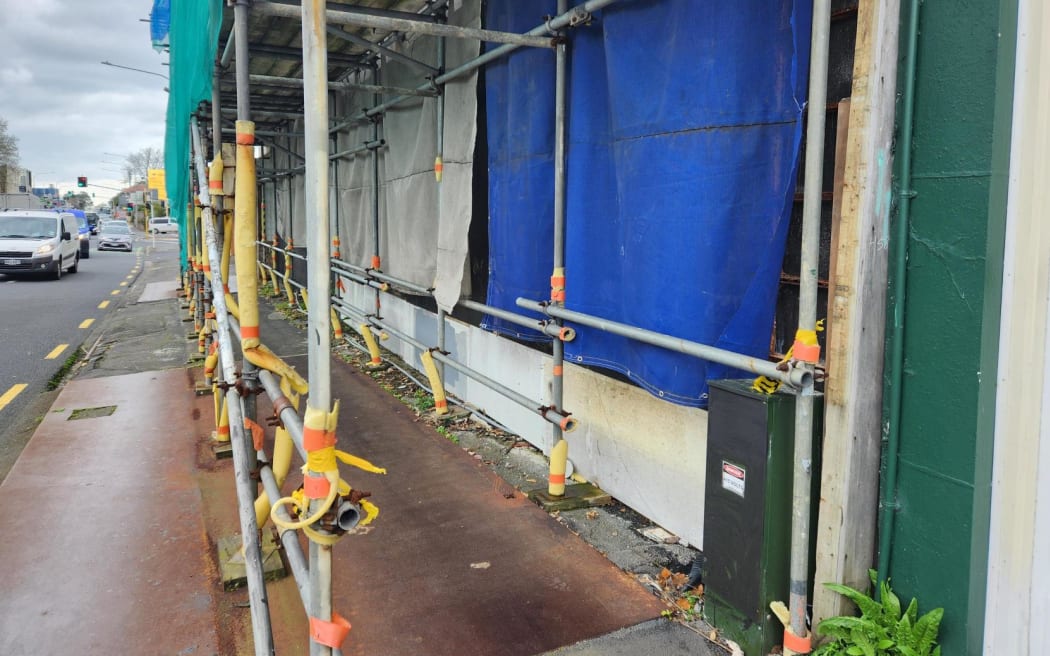 The footpath in front of the unfinished building, covered by scaffolding.