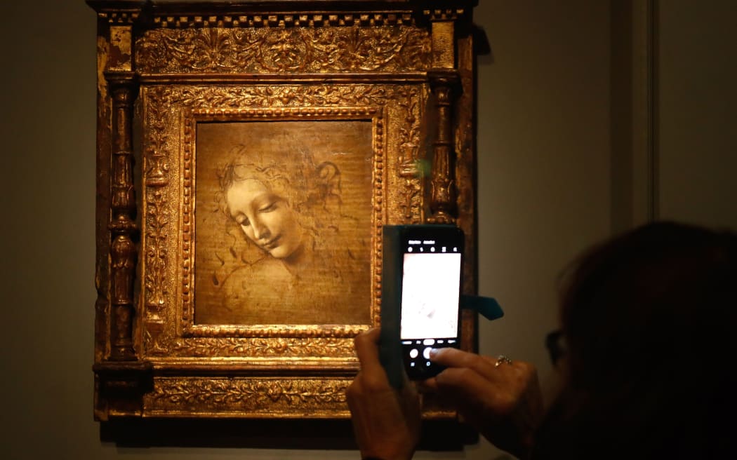 A person take a picture of  an oil on wood painting by Leonardo da Vinci's  " The Head of a Womanalso known as La Scapigliata ",
