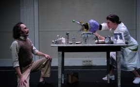 A photo taken of the theatre show 'Death, Ray'. Ray is cowering while an actress animates a death ray machine to speak to Ray.