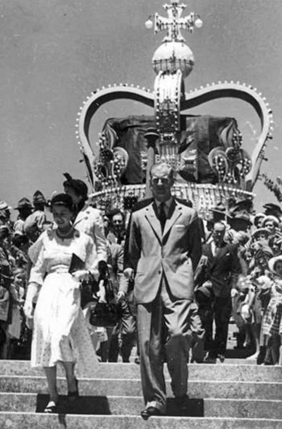 A huge crown dwarfs the royal couple as they walk down the steps in front of Nelson Cathedral, 17 January 1954.