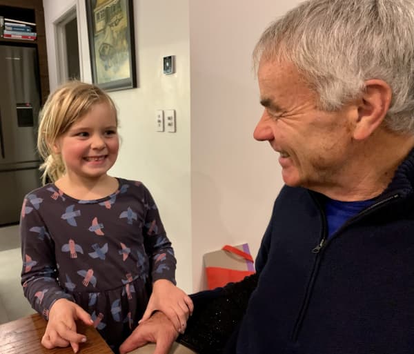 Willa, a young girl with blonde hair, shares a cheeky smile with Tom, her grandfather.
