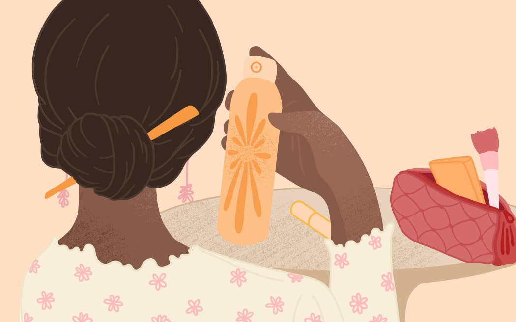 A woman holds up a spray can from a bag of cosmetics.