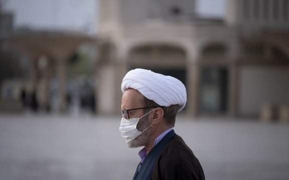 A Iranian cleric wearing a face mask walks near a shrine in the holy city of Qom, March 2020..