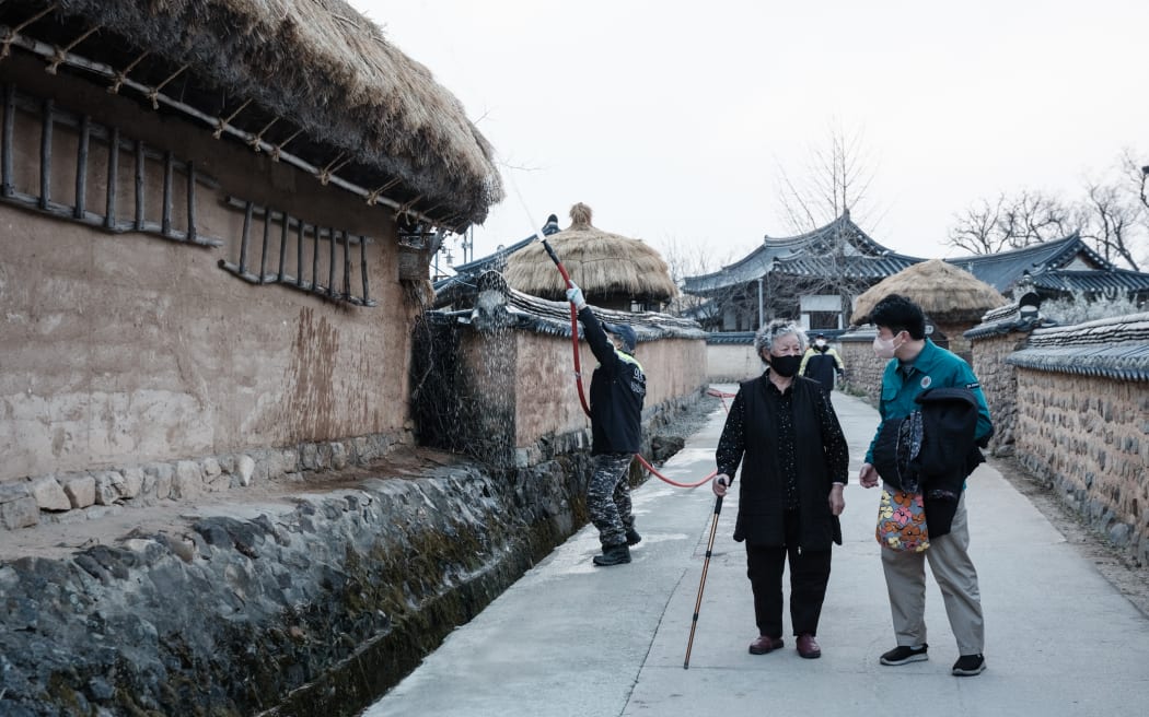 An woman is escorted by a city official as she evacuates from her home due to the approaching wildfire in Andong Hahoe Folk Village, in Andong, South Korea, on 25 March 2025. Inhabitants of a UNESCO-listed village were ordered to evacuate while a historic Buddhist temple was burned to the ground as South Korea scrambled to contain worsening wildfires, which are tearing across the country's southeast.