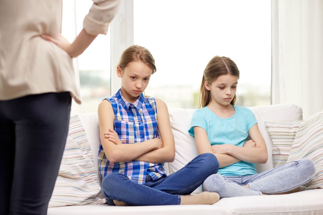 A photo of two girls sitting on the couch and looking chastened after a lecture from their mother