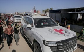 People gather around vehicles of the International Committee of the Red Cross (ICRC) in Khan Yunis, southern Gaza Strip, on October 26, 2025. Search operations are underway in the Gaza Strip to locate and recover the bodies of Israeli captives as part of the cease-fire and prisoner-hostage exchange deal between Hamas and Israel. Representatives from Hamas’ armed wing, the Izz al-Din al-Qassam Brigades, and the ICRC met in Khan Yunis to coordinate the recovery efforts. (Photo by Abdelrahman Rashad / Middle East Images via AFP)