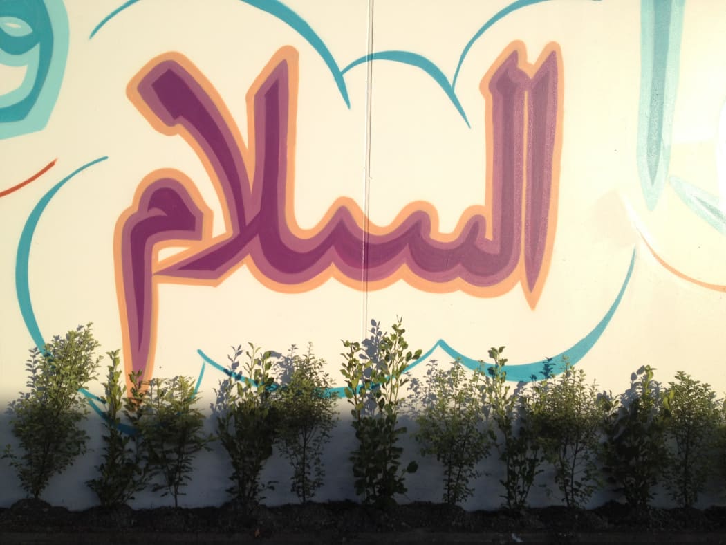 Plants in commemoration of the 51 lives lost in the Christchurch mosque shootings are put at Linwood Mosque underneath a mural of a saying from the Prophet.