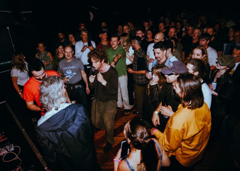 People crowd around a brown-haired male singer who stands among the audience at a live music gig.