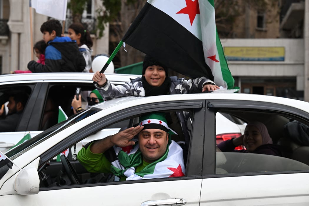A boy waves a Syrian flag as they celebrate a year since the ousting of longtime ruler Bashar al-Assad in the Syrian capital Damascus on December 8, 2025. President Ahmed al-Sharaa on December 8 urged Syrians to work together to rebuild their country as they marked a year since the ousting of longtime ruler Bashar al-Assad. Sharaa's Islamist-led alliance launched a lightning offensive in late November last year, taking the capital Damascus on December 8 after nearly 14 years of war and putting an end to more than five decades of the Assad family's iron-fisted rule. (Photo by LOUAI BESHARA / AFP)