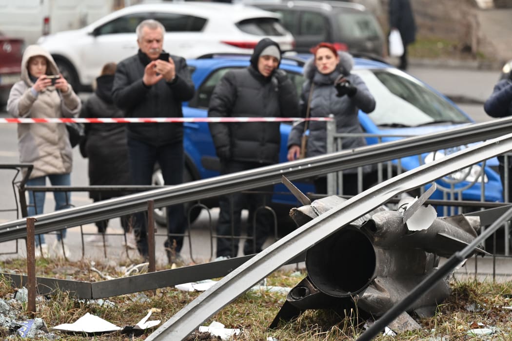 People react standing behind the cordoned off area around the remains of a shell in Kyiv on February 24, 2022.