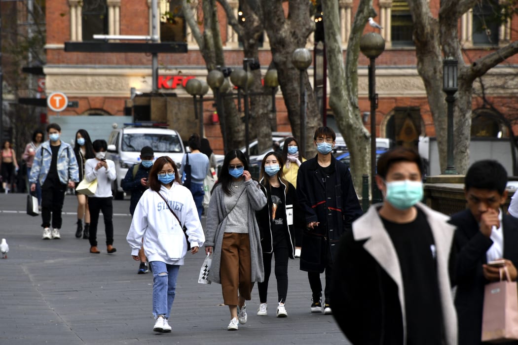 People wearing face masks walk on a street in the central business district of Sydney on August 3, 2020.