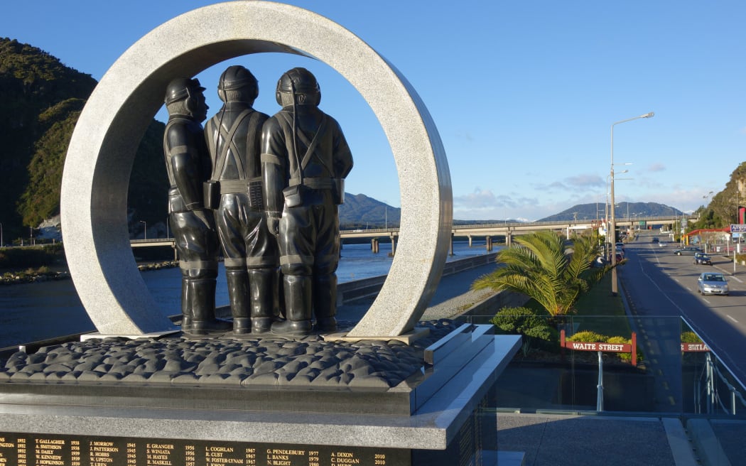 Upright stone circle encloses 3 men in mining gear on top of memorial to  those lost to mining accidnets