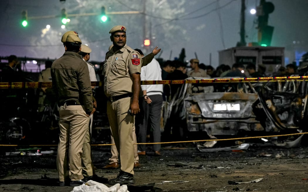 Police personnel stand beside charred vehicles at the blast site after an explosion near the Red Fort in the old quarters of Delhi on November 10, 2025. Indian fire officers on November 10, reported injuries after fire engulfed several vehicles close to the capital's landmark Red Fort, but the cause of the blaze was not confirmed. (Photo by Sajjad HUSSAIN / AFP)