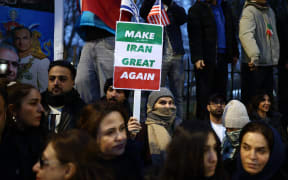 Anti-Iranian regime protesters wave Iranian flags during a gathering outside the Iranian Embassy, central London, on January 12, 2026. (Photo by Henry NICHOLLS / AFP)