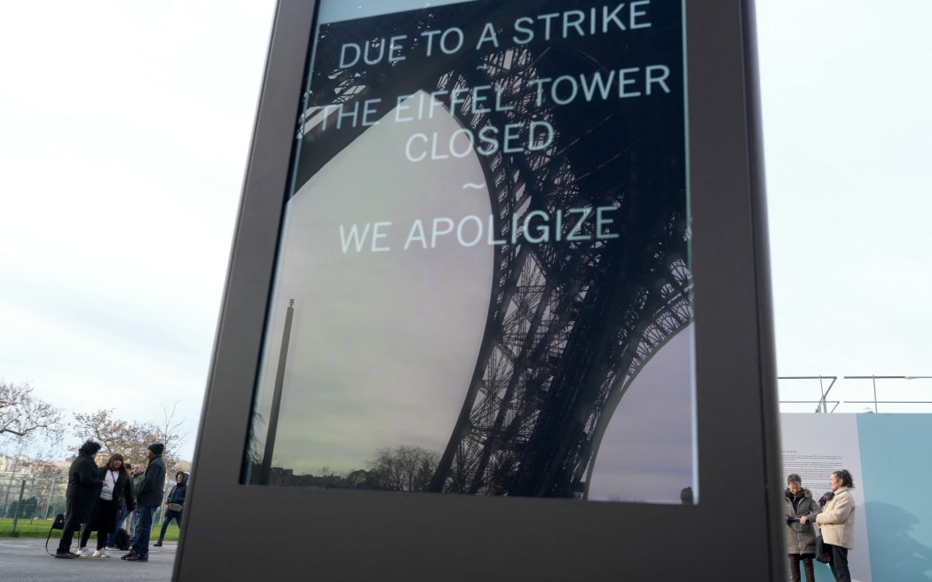 This photograph taken on December 27, 2023 in Paris shows tourists behind a board informing visitors that the Eiffel Tower is closed after staff went on strike. The strike on the 100th anniversary of the death of engineer Gustave Eiffel, who built the tower, was to protest about "the current way it is managed", the hard-left CGT union said in a statement. (Photo by Dimitar DILKOFF / AFP)