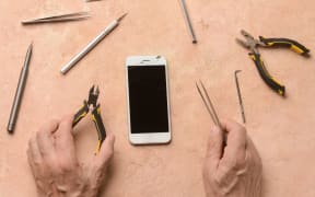 Male technician repairing damaged mobile phone on colour background.