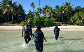 Crew members from Royal New Zealand Navy inshore patrol vessel HMNZS Taupo and personnel from Fiji Revenue and Customs Service wade towards the remote island where over 12 kgs of cocaine were found last week.