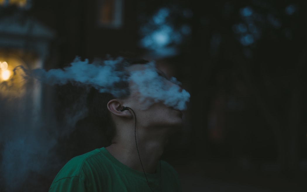 Young man with vape, vaping, blowing a vape cloud.