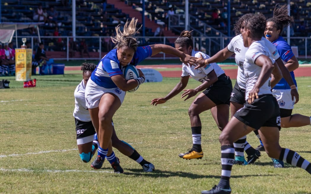 An image of a Samoan women's player running with the ball as Fijian Players try to tackle her.