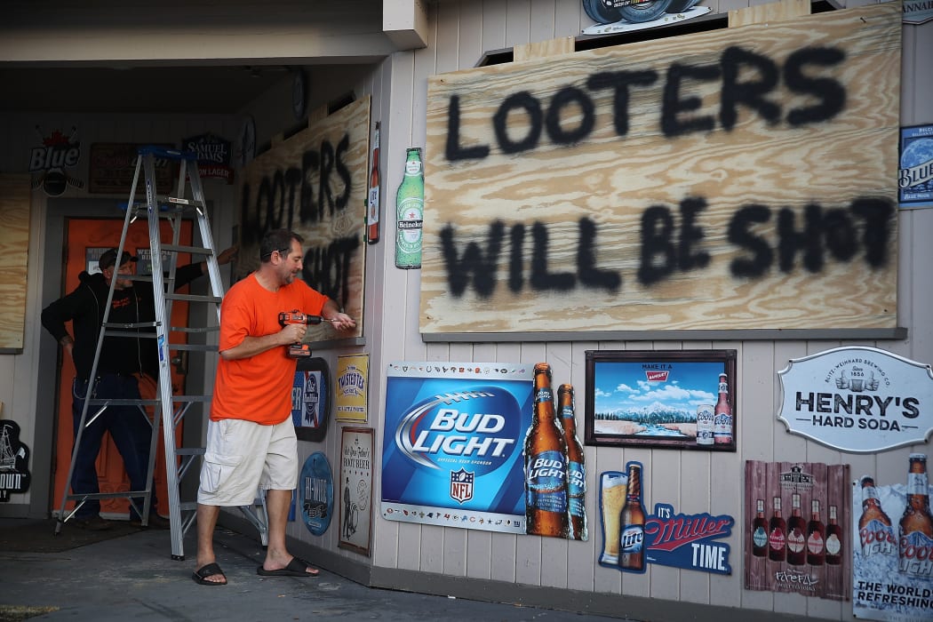Doug Lewis (L) and Chris Williams use plywood with the words 'Looters will be shot' to cover the windows of Knuckleheads bar as they try to protect the business ahead of the arrival of Hurricane Florence.