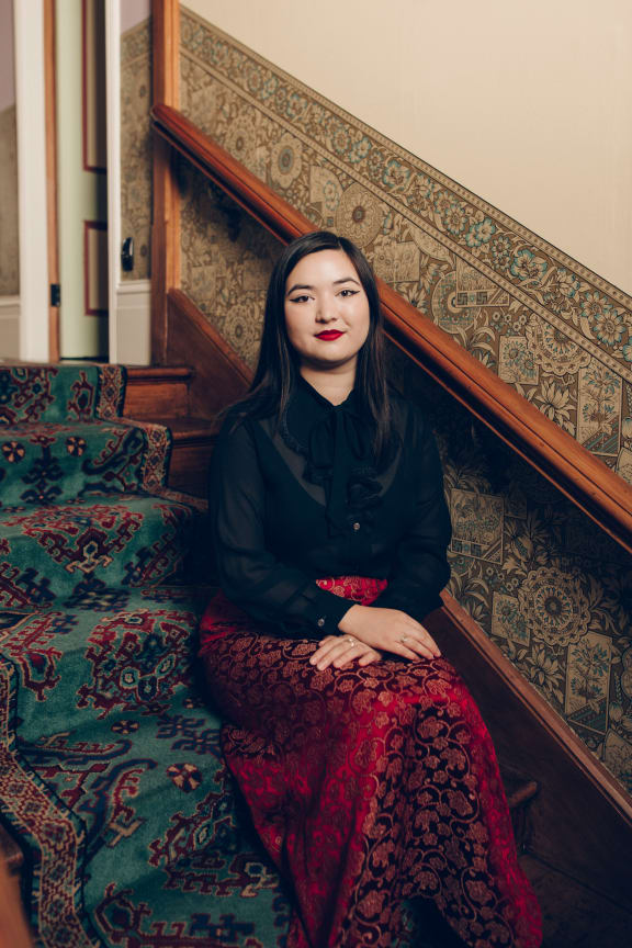 Cadence Chung sits on a staircase, next to a wall with decorative wallpaper in the lower part.