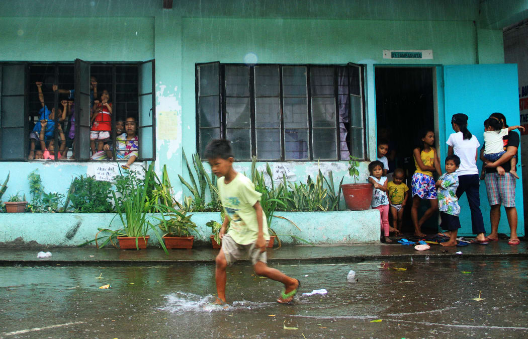 A young evacuee wades through flooded school grounds while others look on from a school building being used as an evacuation center in the city of Legaspi in Albay province, south of Manila on December 14, 2015,