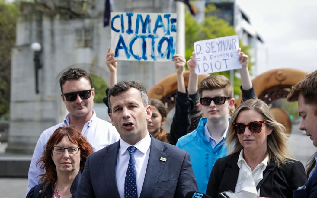 ACT leader David Seymour speaks to media with two teenage protesters standing behind him on 10 October, 2023