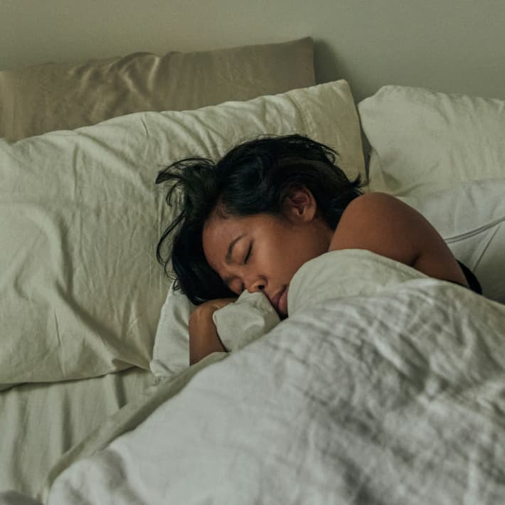 A woman with black hair curls up asleep in bed.