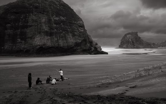A group of people sit on a beach in a circle listening to a high performance coach.