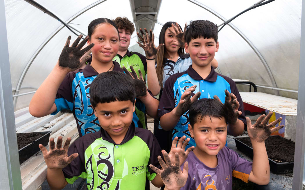 Students at Te Pā O Rākaihāutū stand in a group smiling at the camera hold their hands which are covering in dirt from gardening.