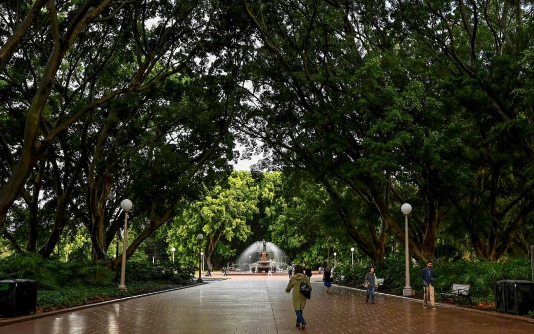 A woman walks through Hyde Park on a rainy day after office hours in the central business district in Sydney on May 10, 2024. (Photo by Saeed KHAN / AFP)
