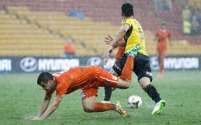 Roar forward Andrija Kaluderovic (left) falls over in the rain as Phoenix defender Michael Boxall (right) chases the ball.