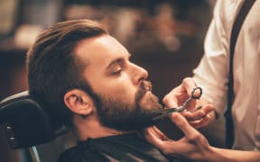 Close-up side view of young bearded man getting beard at barber shop.