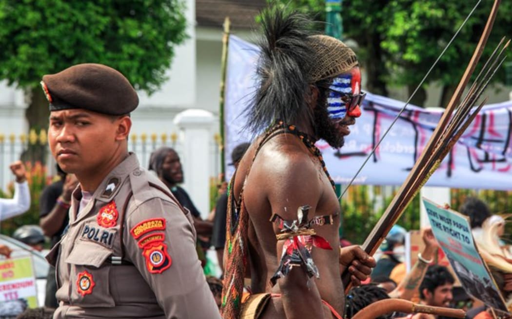 A Papuan man (right) in traditional clothing and face painted with the banned Morning Star flag stands next to a policeman during a demonstration demanding a referendum on independence in Yogyakarta on Dec. 1, 2023.