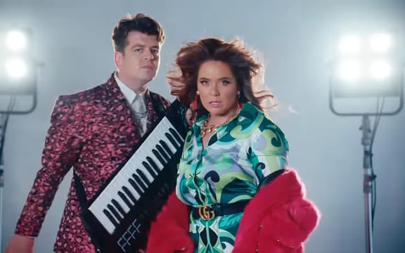 Comedian's Laura Daniel and Joseph Moore standing next to each other. Moore is holding his keyboard. Both are wearing glamourous clothes and makeup.