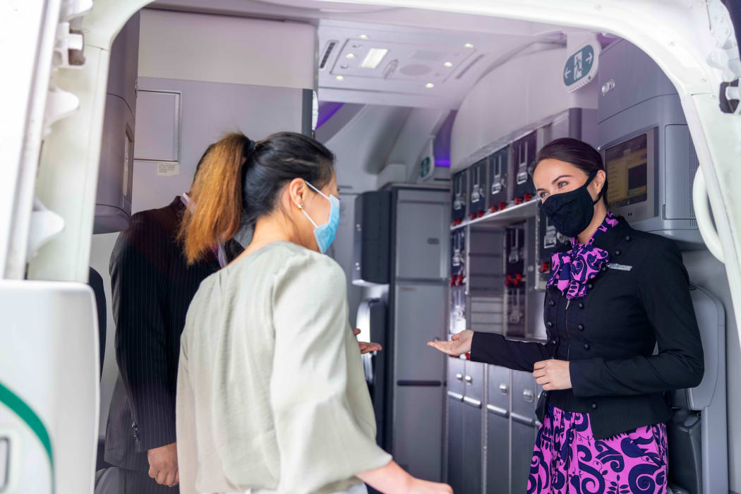 A flight attendant welcomes passengers onto an Air New Zealand flight.