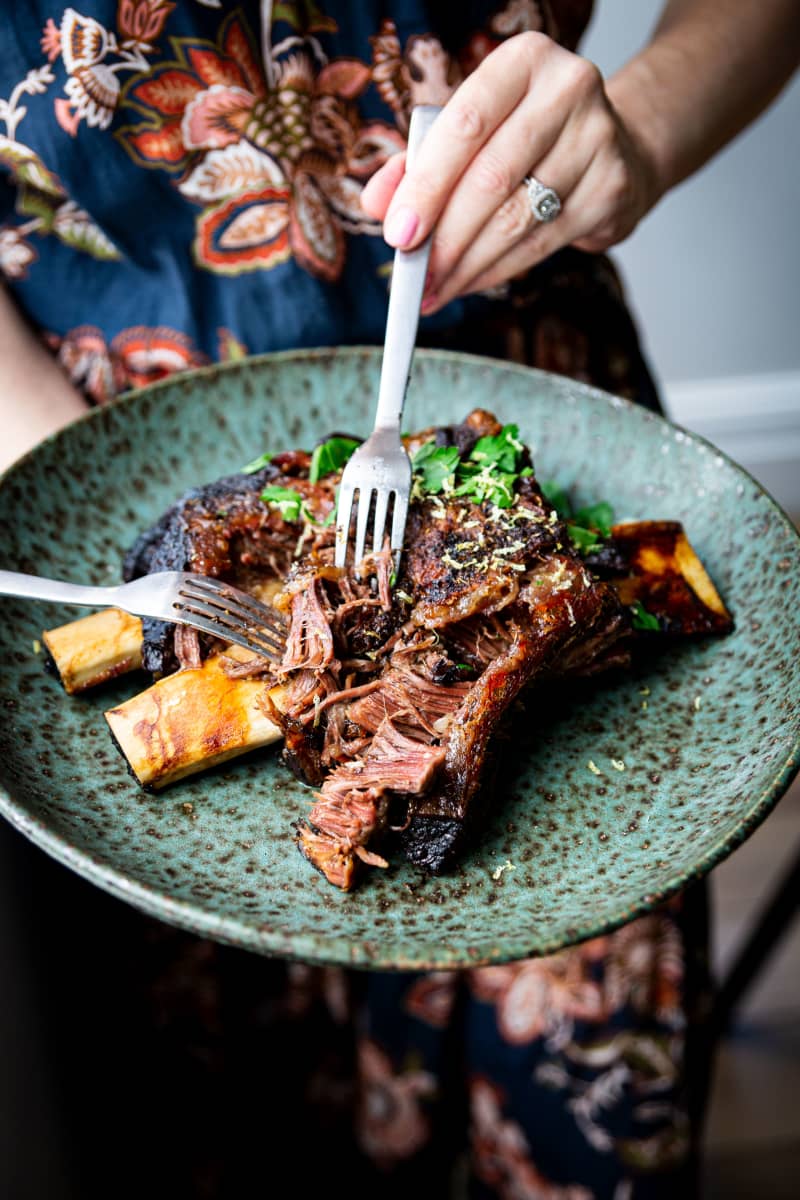 A plate of slow cooked short ribs, being pulled apart by two forks.