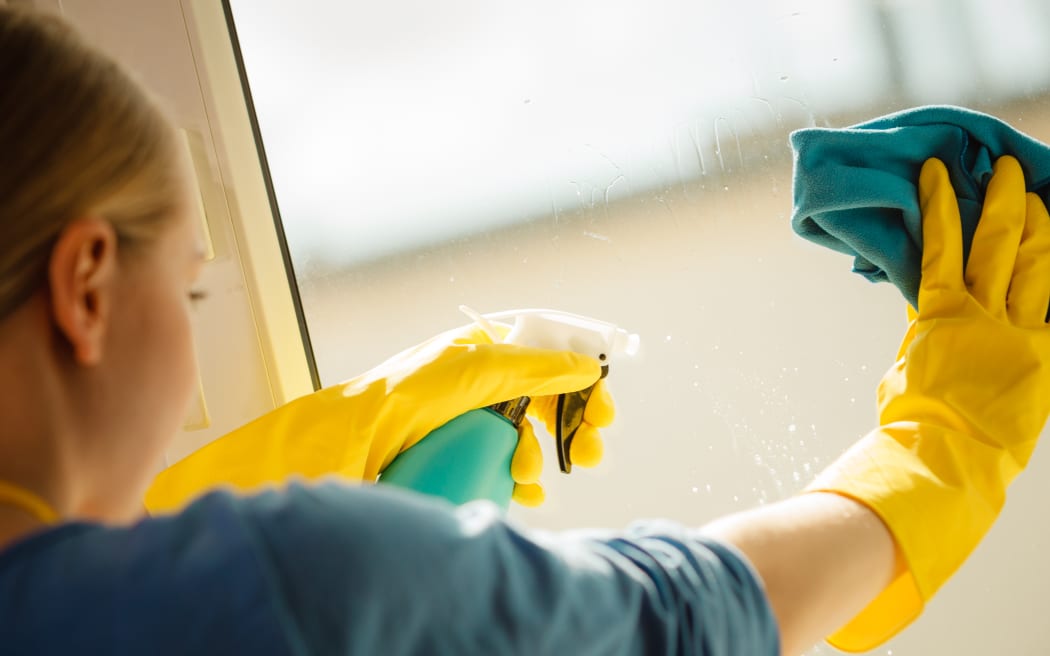 Young woman in yellow gloves cleaning window with blue rag and spray detergent. Spring cleanup, housework concept