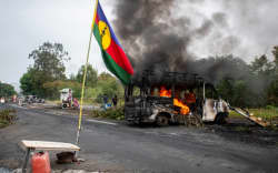 This photograph shows a Kanak flag waving next to a burning vehicle at an independantist roadblock at La Tamoa, in the commune of Paita, France’s Pacific territory of New Caledonia on May 19, 2024. French forces smashed through about 60 road blocks to clear the way from conflict-stricken New Caledonia’s capital to the airport but have still not reopened the route, a top government official said on May 19, 2024. (Photo by Delphine Mayeur / AFP)