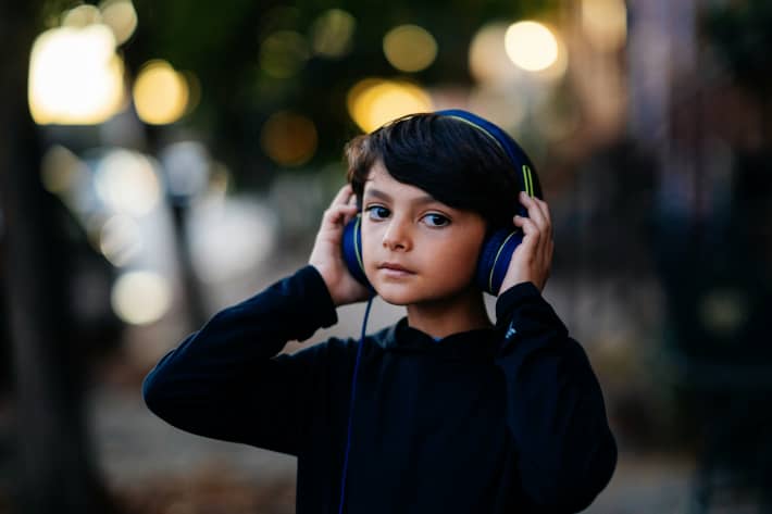 A child listening to headphones, with their hands on each headphone, wearing a dark-coloured top.