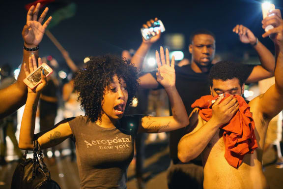 Demonstrators protesting over the killing  try to stand their ground despite being overcome by tear gas.