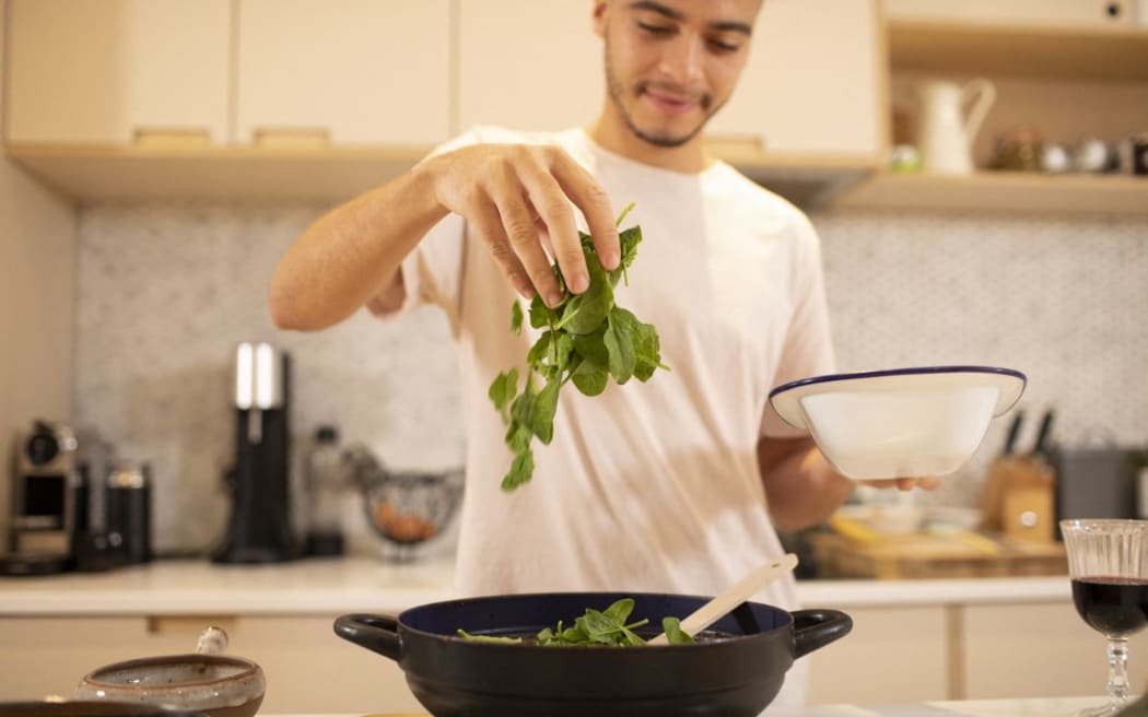 Young man cooking with fresh spinach in kitchen. (Photo by Sam Edwards/CAIA IMAGE/SCIENCE P / NEW / Science Photo Library via AFP)