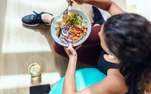 Shot of sporty young woman eating healthy while listening to music sitting on the floor at home.