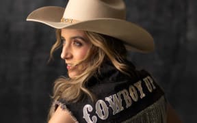Kaylee Bell wears a vest that reads cowboy and a cowboy hat.