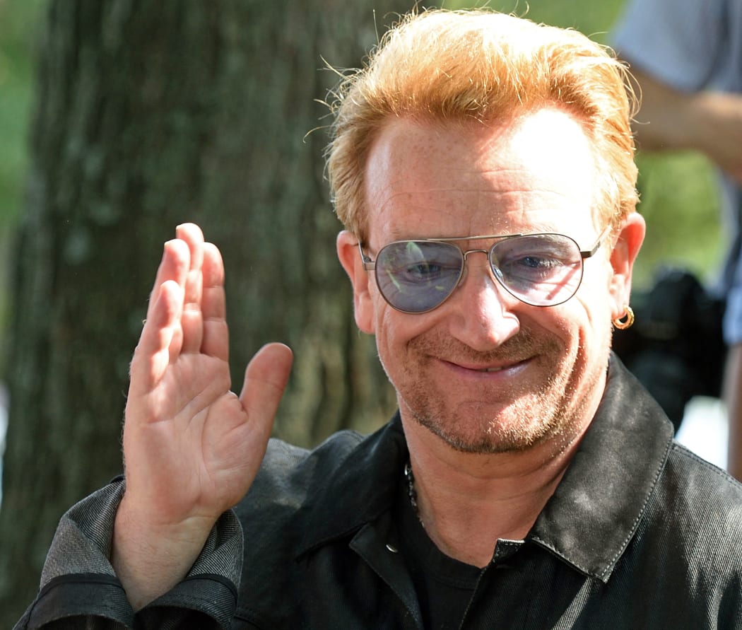 Bono waves during a dedication ceremony for a giant tapestry, from Amnesty International, in honor of John Lennon on Ellis Island 29 July 2015 in New York.